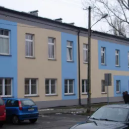 Odnowiona elewacja budynku wielorodzinnego z podziałem na beżowe i błękitne segmenty, widoczne samochody osobowe na pierwszym planie.