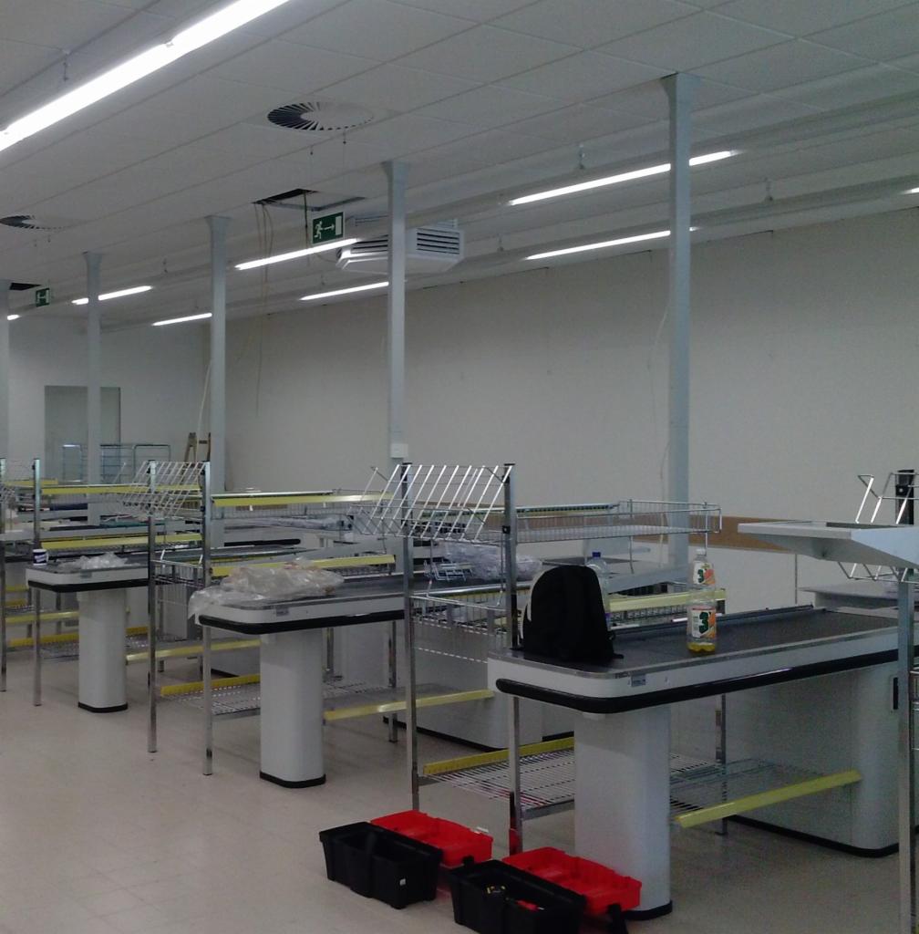 Nowe stanowiska kasowe w supermarkecie, częściowo zmontowane, z widocznymi narzędziami w skrzynkach na podłodze i torbą na jednym z blatów.