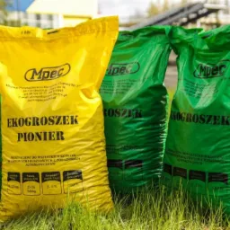 Żółta i zielone worki z ekogroszkiem MPEC Olsztyn, ustawione na trawie. Widoczne parametry opału i oznaczenia producenta.