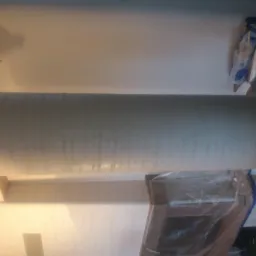 Świeżo pomalowana ściana w jasnym odcieniu szarości, z widocznymi smugami po wałku, zabezpieczone folią ościeżnice drzwiowe, oraz akcesoria malarskie w tle.