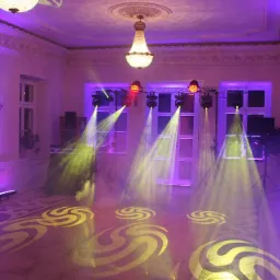 Sala balowa z oświetleniem eventowym: reflektory punktowe tworzą wzory na parkiecie, DJ-ka w tle, fioletowe podświetlenie ścian i okien, kryształowy żyrandol.