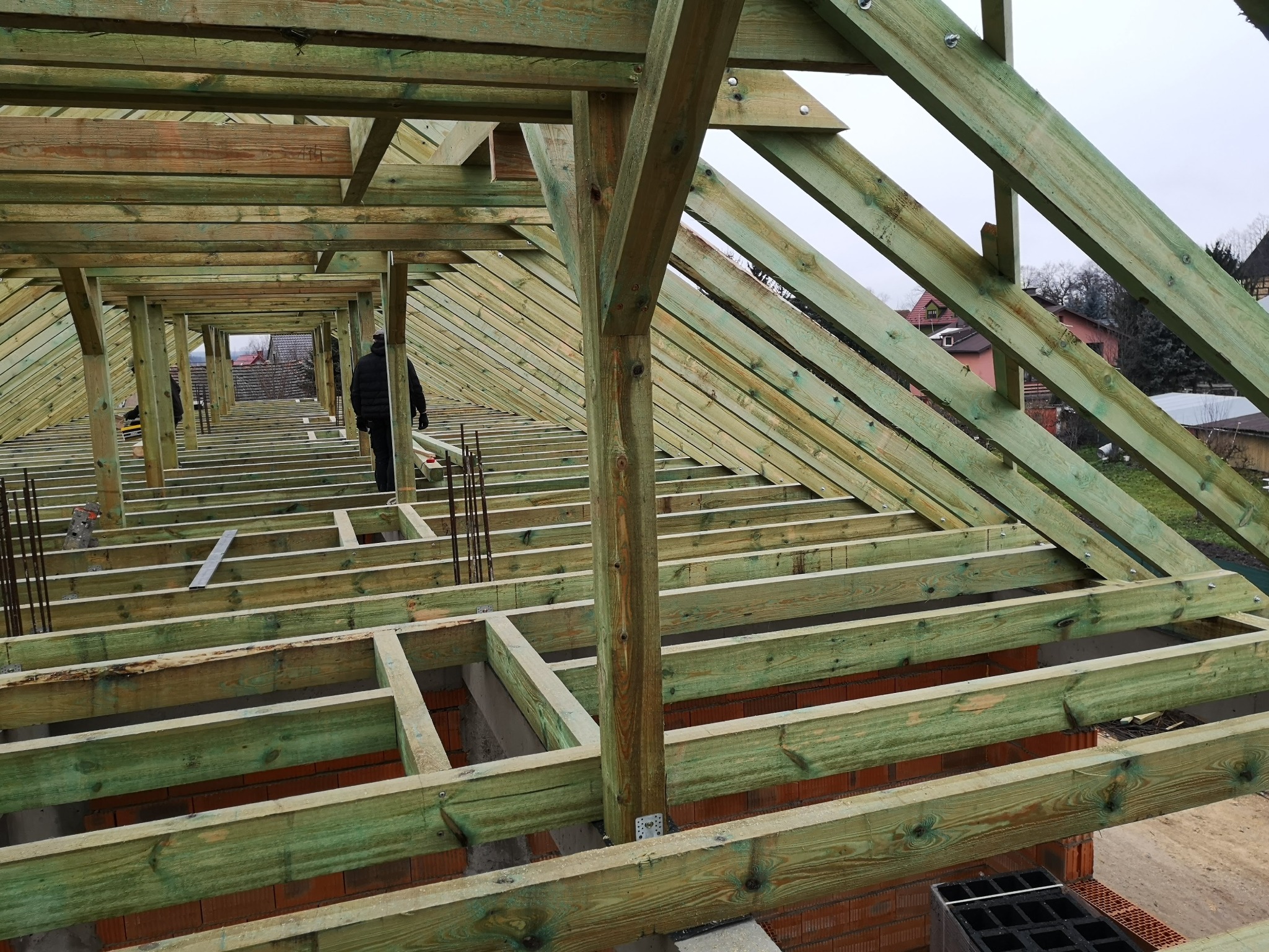 Konstrukcja dachu z impregnowanego drewna w trakcie montażu, widok z góry na surowy szkielet z osobą w oddali. Elementy połączone śrubami.