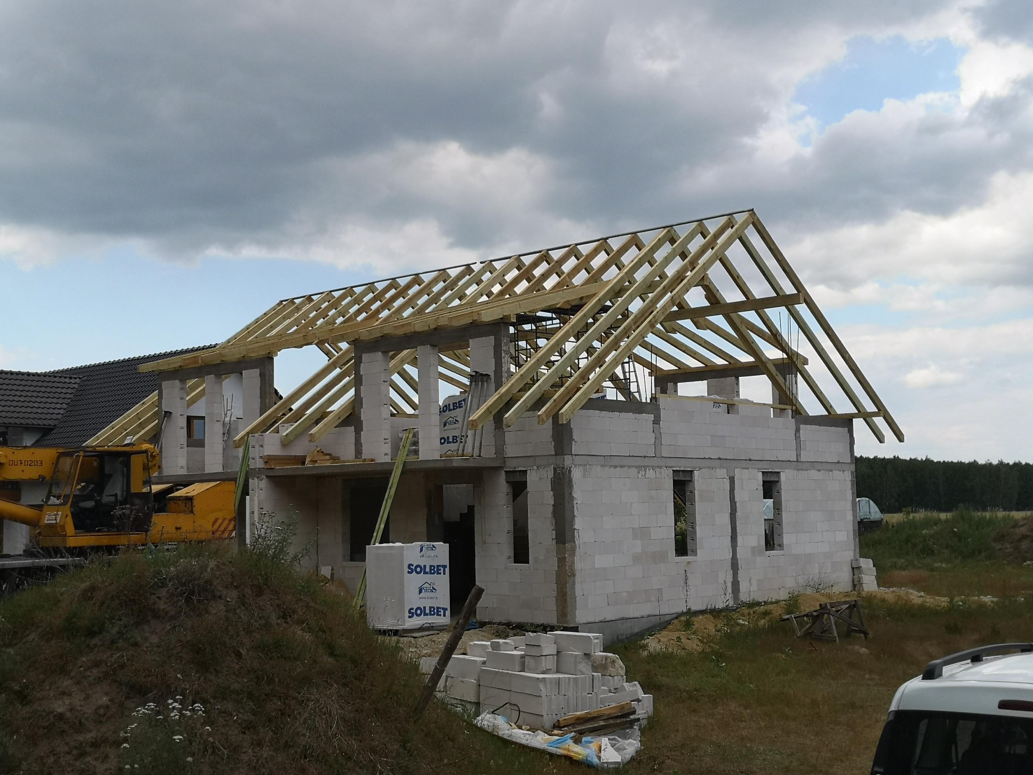 Budowa domu z bloczków Solbet, w trakcie montażu drewnianej konstrukcji dachu, widoczny dźwig budowlany i elementy więźby dachowej.