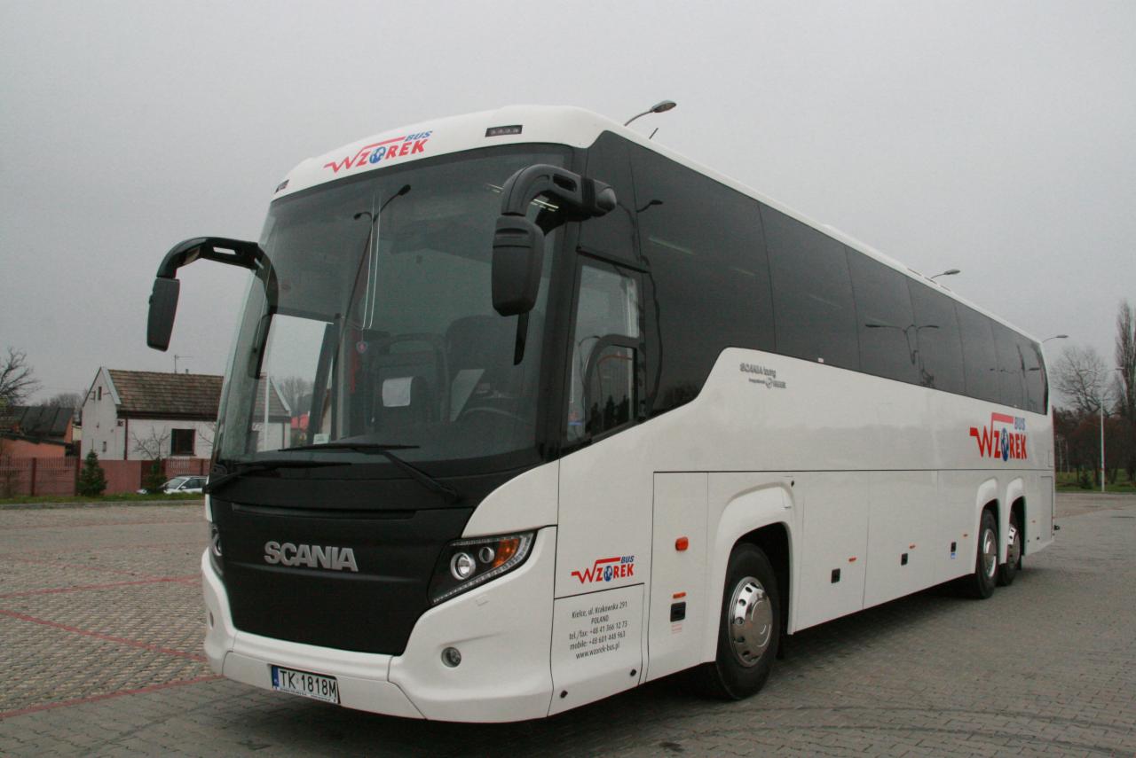 Biały autokar marki Scania z logo 'WZOREK BUS' na parkingu z kostki brukowej w pochmurny dzień.