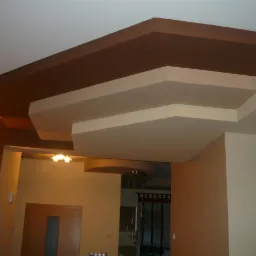 Wielopoziomowy sufit podwieszany z płyt kartonowo-gipsowych, pomalowany na beżowo i brązowo, z widocznym oświetleniem w tle. Dekoracyjne wykończenie wnętrza.