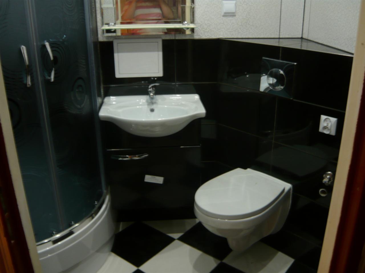 Nowoczesna łazienka z czarno-białą podłogą, kabiną prysznicową i wiszącą toaletą. Umywalka z szafką i czarne płytki na ścianach. Minimalistyczny design.