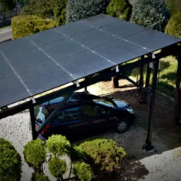 Czarny samochód zaparkowany pod wiatą fotowoltaiczną z panelami monokrystalicznymi, widok z góry, otoczenie zieleni.