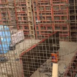 Zbrojenie i szalunek pod wylewkę fundamentów, widoczne pręty stalowe, deski szalunkowe oraz pomarańczowy pojemnik w wykopie.