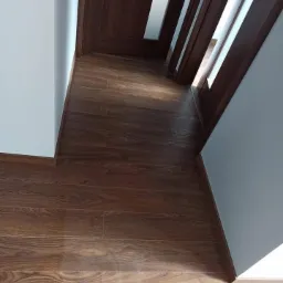 Ukończone schody z brązowymi panelami podłogowymi imitującymi drewno, białe ściany i nowoczesna balustrada w Mieścisku.