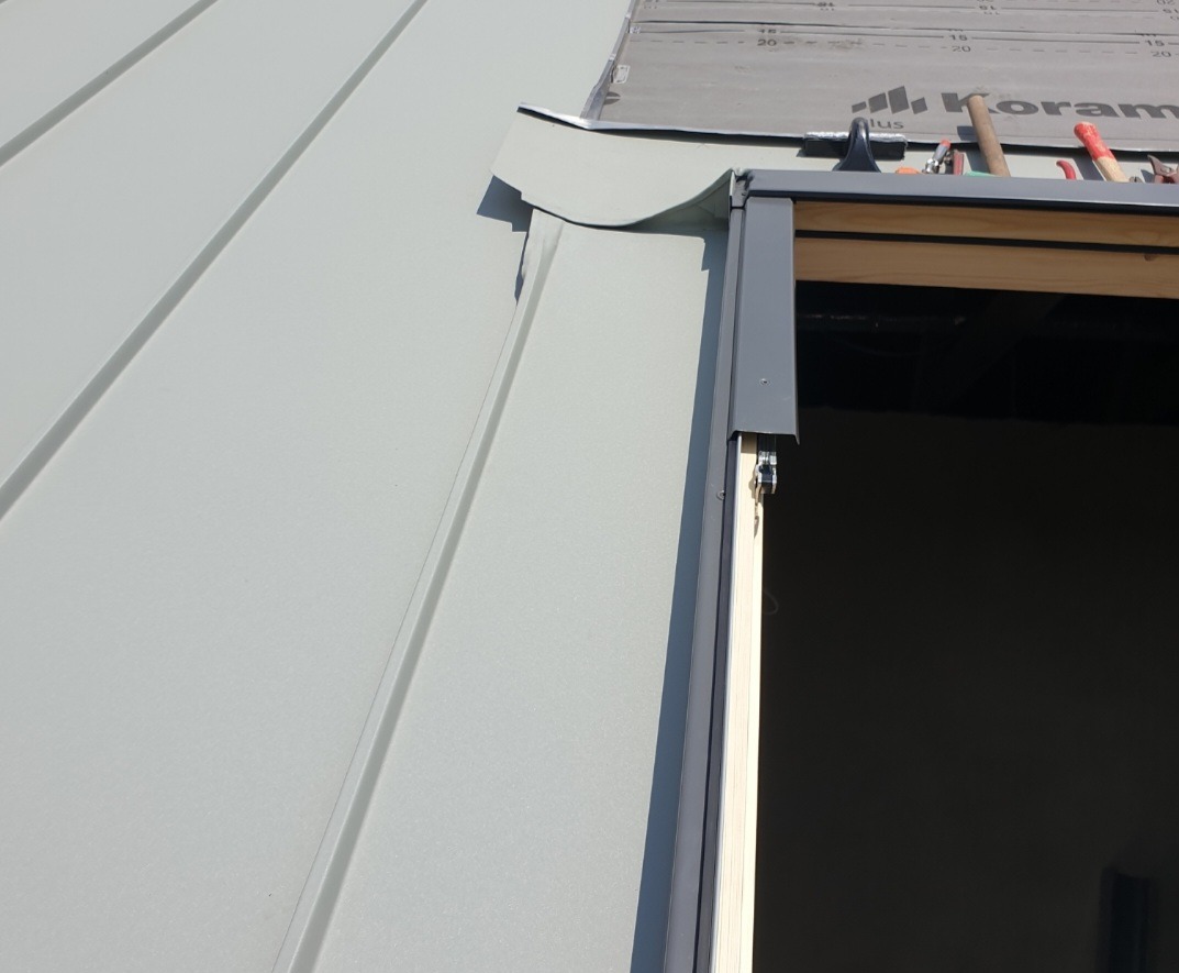 Szary panel dachowy z blachy na dachu w trakcie montażu, widoczne narzędzia i fragment membrany dachowej.