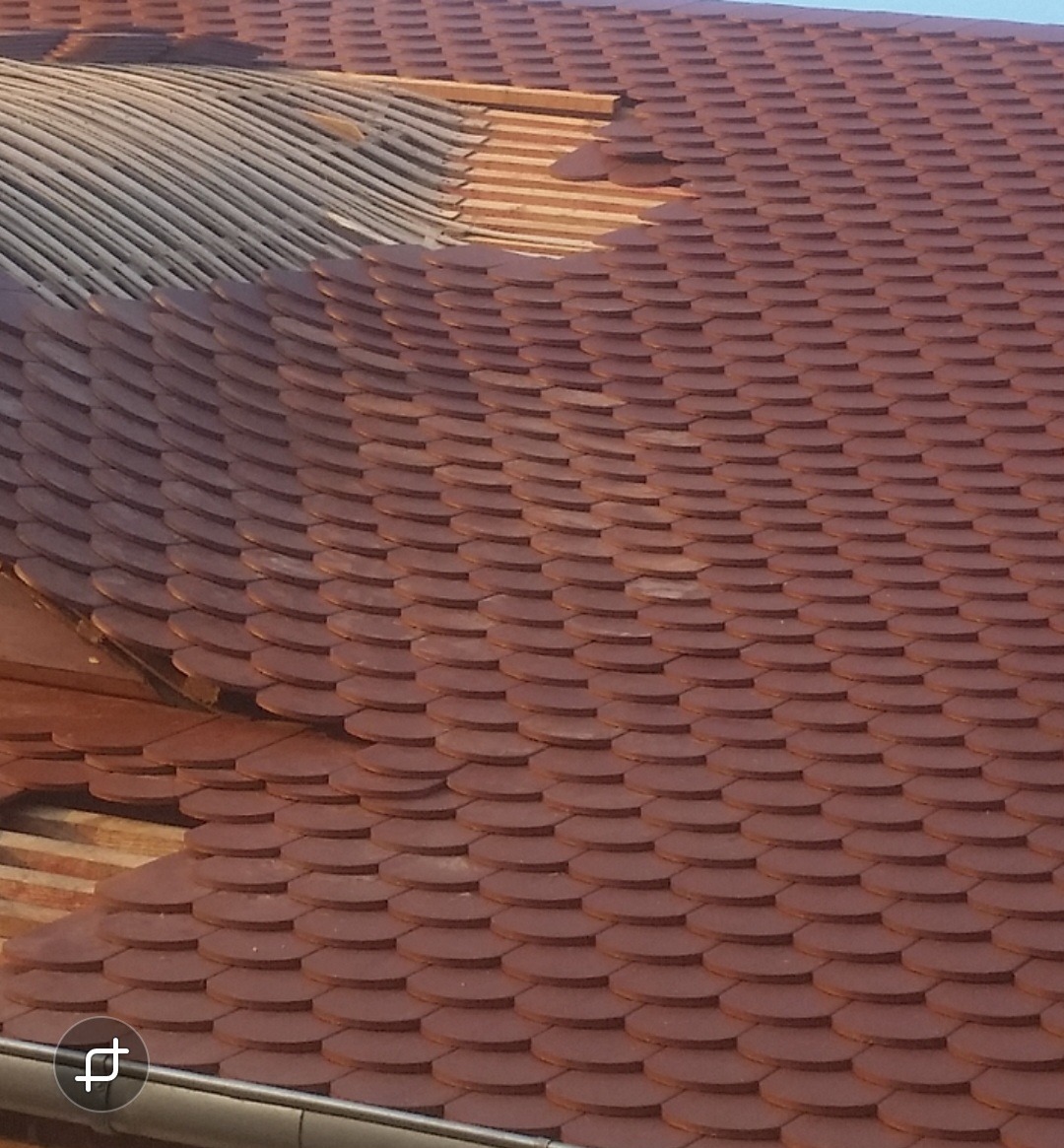 Fragment dachu z brązową dachówką karpiówką; widoczne uszkodzone fragmenty i konstrukcja nośna.