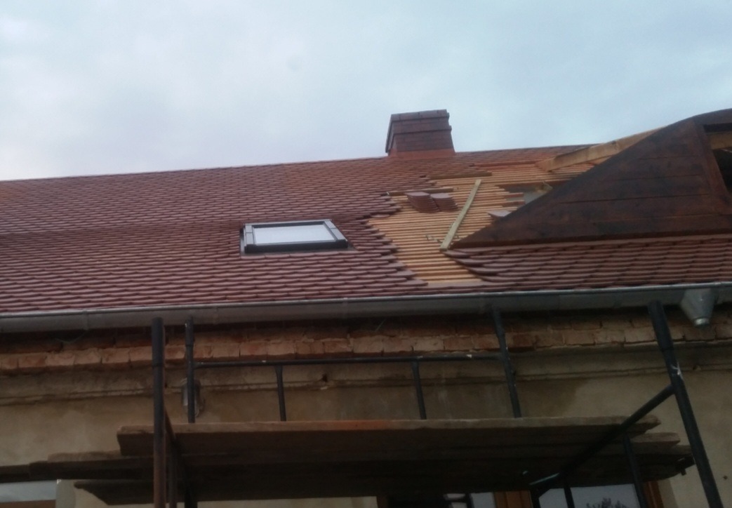 Częściowo zdjęte dachówki na dachu z oknem, widoczny komin i rusztowanie, etap prac.