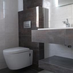 USŁUGI BUDOWLANE Sylwester Kurs - Nowoczesna łazienka z podwieszaną toaletą, umywalką na blacie z szarej płyty i szarymi płytkami na ścianach. Minimalistyczny design, oświetlenie LED.