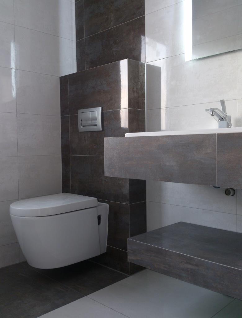 Nowoczesna łazienka z podwieszaną toaletą, umywalką na blacie z szarej płyty i szarymi płytkami na ścianach. Minimalistyczny design, oświetlenie LED.