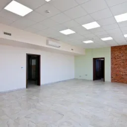Pusta, jasna sala biurowa z marmurową podłogą, sufitem kasetonowym i ścianą z czerwonej cegły, przygotowana do wynajmu jako kawiarenka lub bufet w Gliwicach Sośnicy.