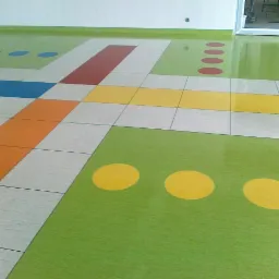 Kolorowa wykładzina podłogowa w przedszkolu z geometrycznymi wzorami: koła, kwadraty i pasy w odcieniach zieleni, żółci, czerwieni, pomarańczy i błękitu.