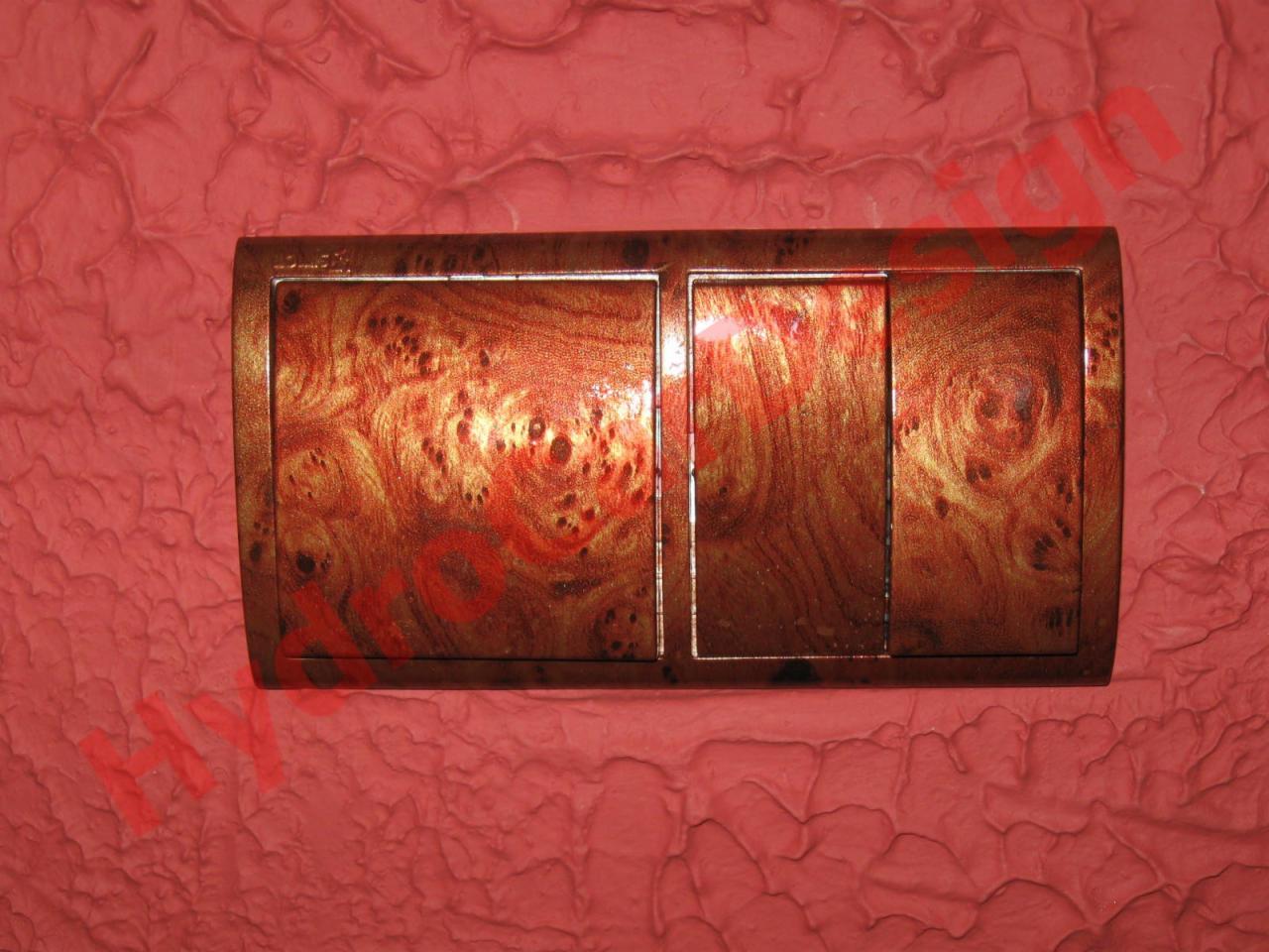 Panel samochodowy z hydrografiką imitującą drewno na tle teksturowanej czerwonej powierzchni.