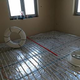 AM-INSTAL Artur Mielko - Rozłożone rury ogrzewania podłogowego na folii izolacyjnej z widocznymi rolkami rur w nowym pomieszczeniu, przygotowane do zalania wylewką.