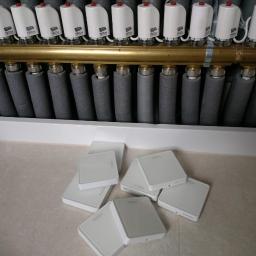 AM-INSTAL Artur Mielko - Rozdzielacz ogrzewania podłogowego z termostatami i izolowanymi rurami, obok leżą białe sterowniki TECH przed montażem.