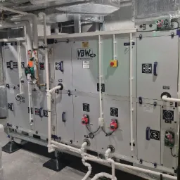 Duża centrala wentylacyjna z licznymi przewodami i elementami sterującymi w pomieszczeniu technicznym, widoczne logo VBW na obudowie.