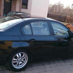 Diamentowy Blask - Błyszczący, czarny sedan BMW po umyciu na kostce brukowej. Widoczne refleksy światła na karoserii, garaż w tle. Auto zaparkowane na posesji.