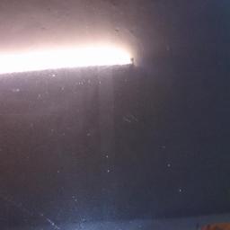 Diamentowy Blask - Błyszcząca, ciemna powierzchnia z widocznymi smugami i odbiciami światła, prawdopodobnie karoseria samochodu po polerowaniu, z fragmentem emblematu Mercedes-Benz.