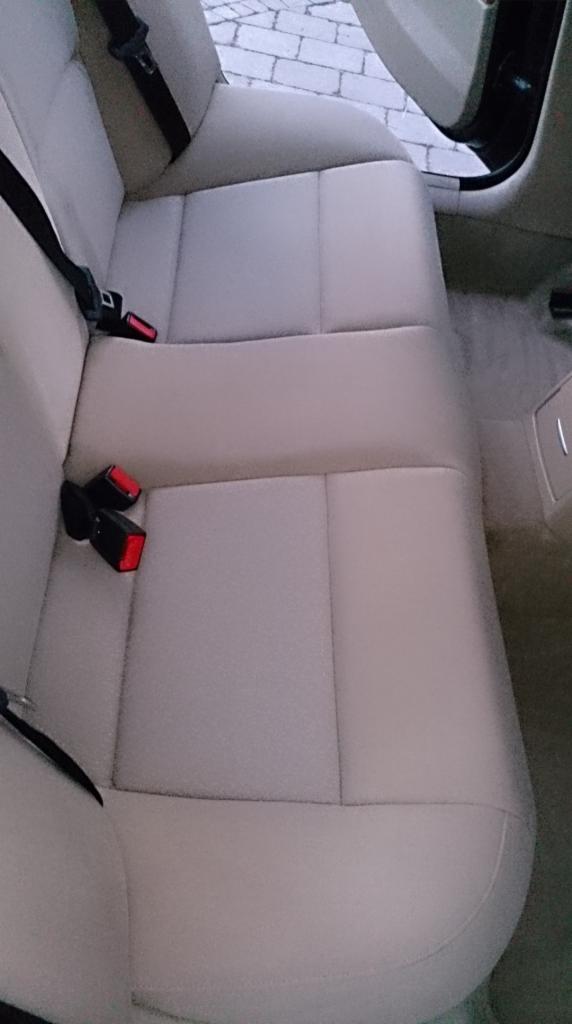 Jasna, skórzana tylna kanapa samochodu z widocznymi pasami bezpieczeństwa. Czyste, zadbane wnętrze pojazdu. Widok z góry.