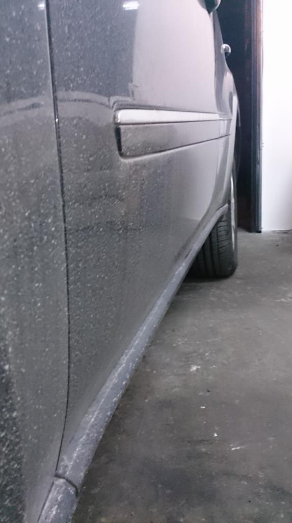 Boczny widok bardzo brudnego, ciemnego samochodu z widocznymi zabrudzeniami na karoserii i oponach, stojącego w garażu.