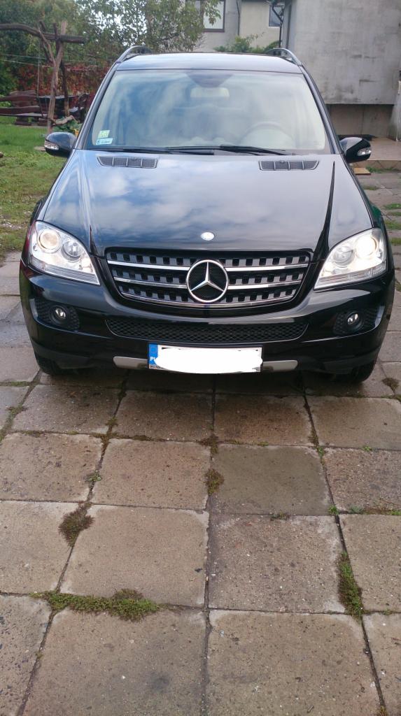 Czarny Mercedes ML, widok z przodu, na kostce brukowej z mchem. Reflektory włączone, tablica rejestracyjna zasłonięta.