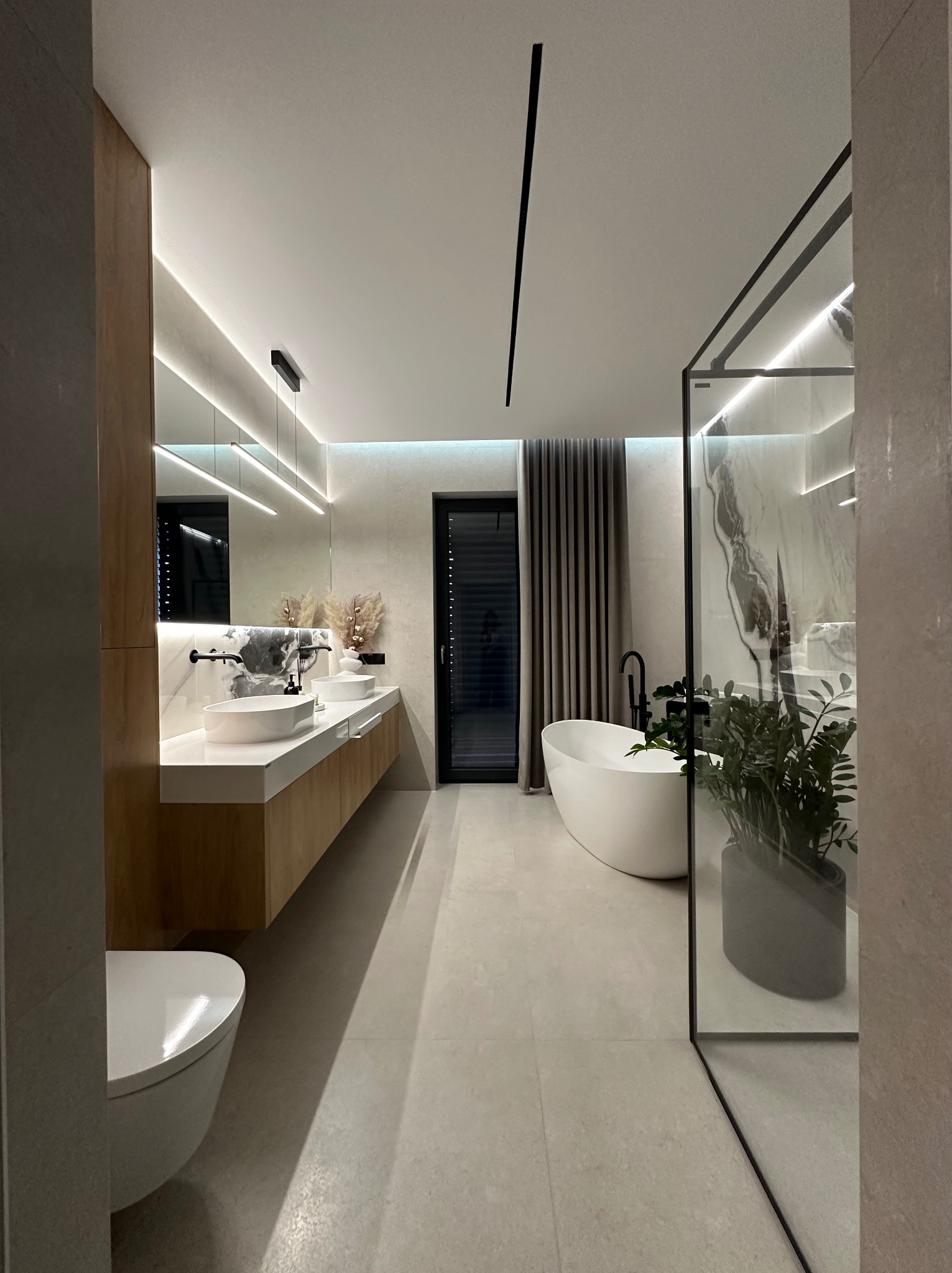 Nowoczesna łazienka z wolnostojącą wanną, umywalkami nablatowymi i kabiną prysznicową typu walk-in. Minimalistyczne oświetlenie LED i neutralna kolorystyka.