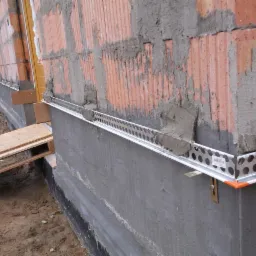 Przygotowanie ściany z pustaków ceramicznych do ocieplenia, widoczny cokół z zamocowanymi profilami startowymi i warstwą wyrównującą zaprawy.