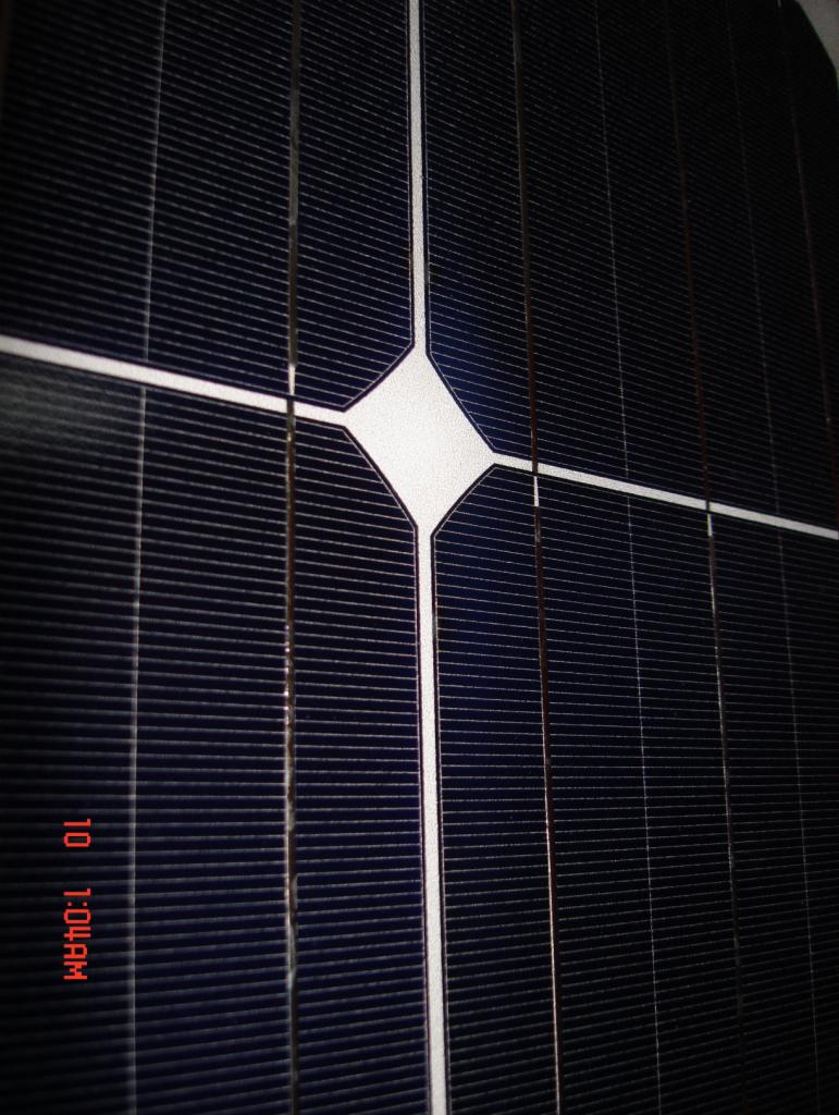 Fragment panelu fotowoltaicznego z widoczną strukturą krzemową i białymi liniami przewodzącymi, uchwycony pod kątem z widocznym stemplem daty 10:04 AM.