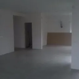 Surowe wnętrze domu w trakcie prac wykończeniowych; widoczne ściany po szpachlowaniu, szary betonowy podkład podłogowy, przygotowane otwory drzwiowe i okienne, płyta gipsowo-kartonowa oparta...