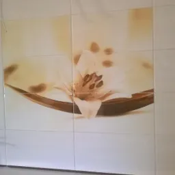 Ściana wyłożona białymi płytkami ceramicznymi z nadrukiem przedstawiającym lilię w odcieniach beżu i brązu.