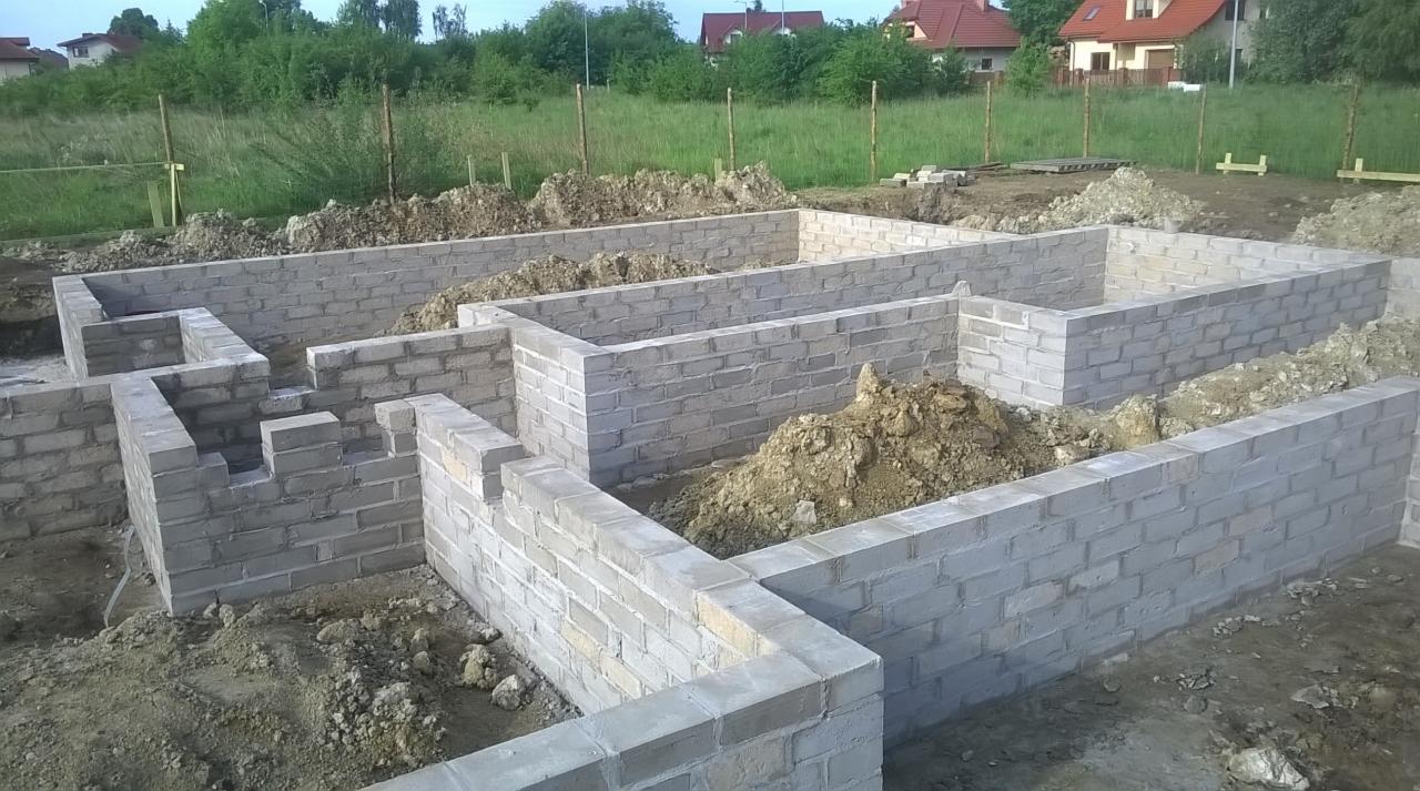 Wznoszenie fundamentów z bloczków betonowych na działce. Widoczne ściany fundamentowe, ziemia i trawa w tle. Budowa w toku, z dbałością o detale.