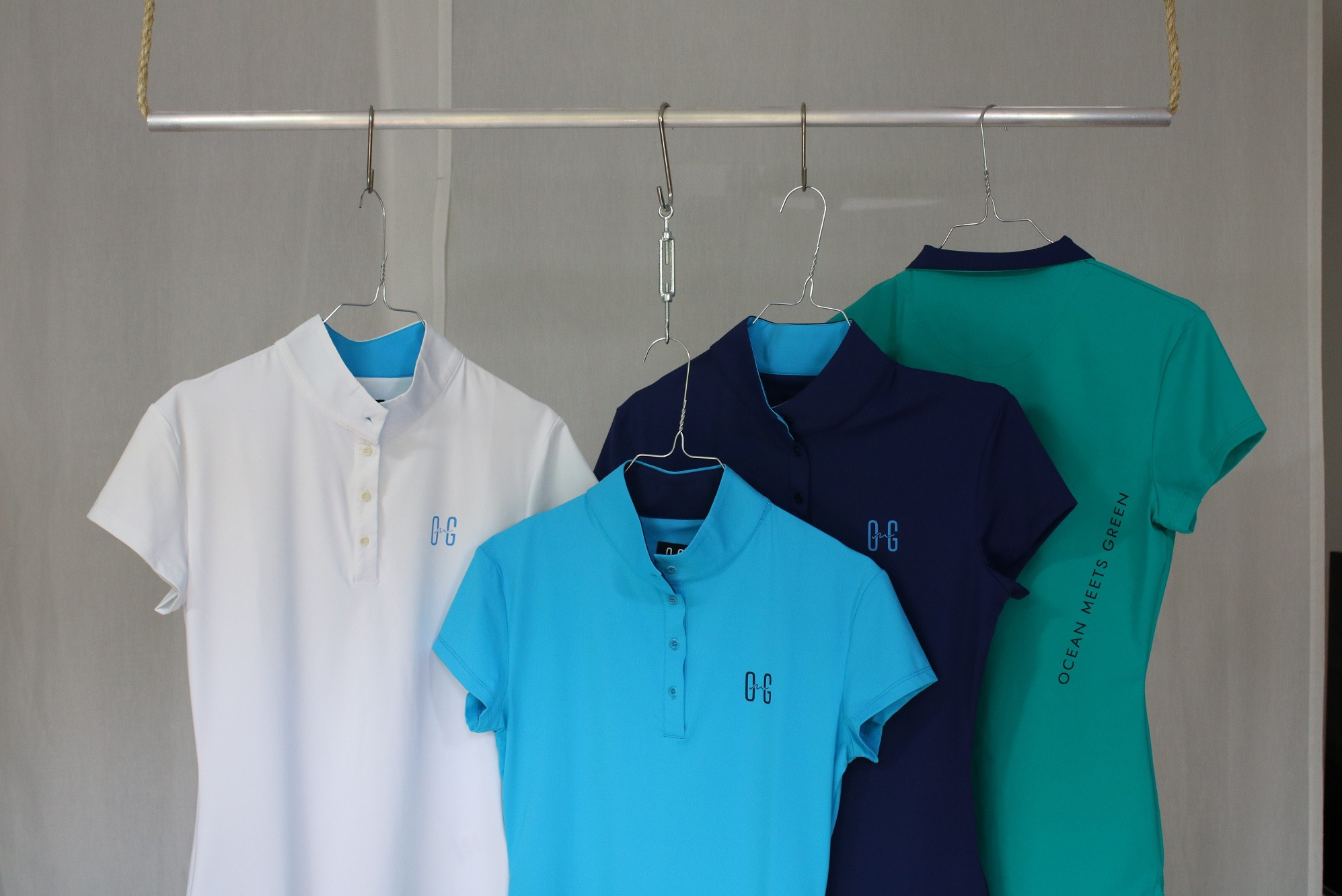 Kolekcja kolorowych koszulek polo z krótkim rękawem, wiszących na metalowym drążku z wieszakami, prezentacja odzieży z logo.