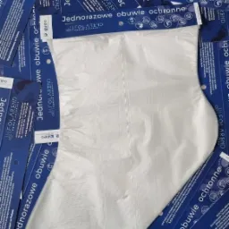 Jednorazowe, białe ochraniacze na obuwie od firmy Folarend, rozłożone na tle niebieskich ulotek z logo i informacjami o produkcie.