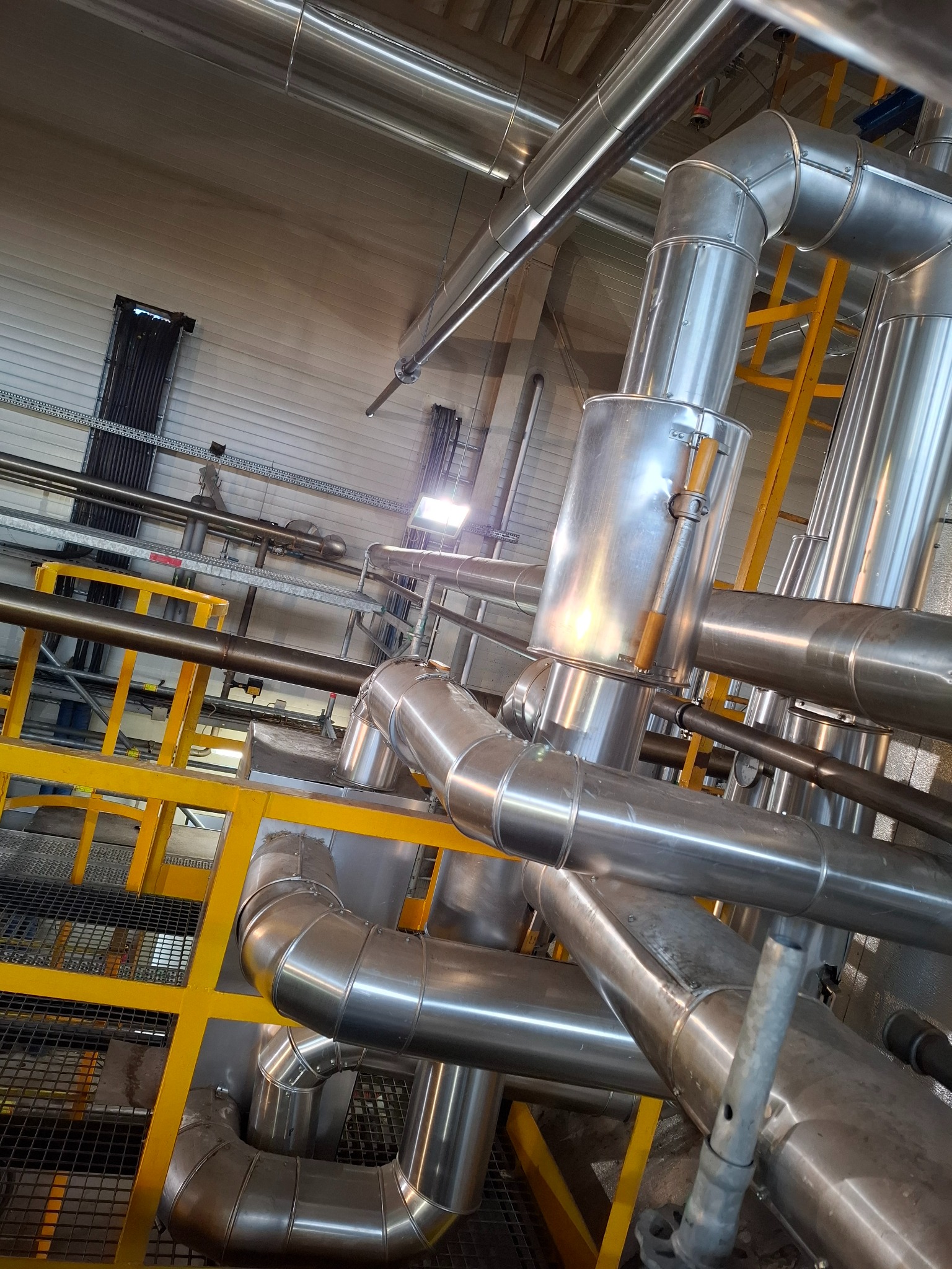 System rur przemysłowych ze stali nierdzewnej z żółtą konstrukcją wsporczą, widok z dołu, oświetlenie sufitowe.