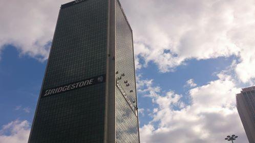 Wieżowiec Bridgestone w Tokio, z widocznymi platformami do mycia okien, na tle błękitnego nieba z chmurami. Ujęcie z dołu.