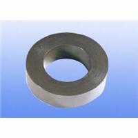 Metalowy pierścień z otworem w środku, o gładkiej, szarej powierzchni, ustawiony pod kątem na niebieskim tle.