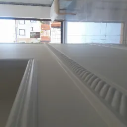 Świeżo pomalowana, biała ściana z dekoracyjnym sztukateryjnym paskiem w Skarżysko-Kamiennej, widok na okno i fragment podłogi z płytek.