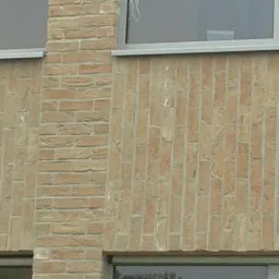 Fragment elewacji budynku z cegły klinkierowej w odcieniach beżu i brązu, z widocznymi oknami z szarą ramą.