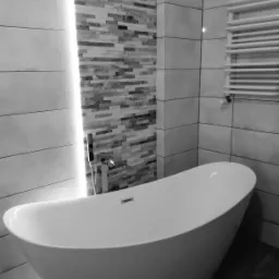 Nowoczesna łazienka w odcieniach szarości z wolnostojącą wanną, mozaiką na ścianie podświetloną listwą LED i grzejnikiem drabinkowym.