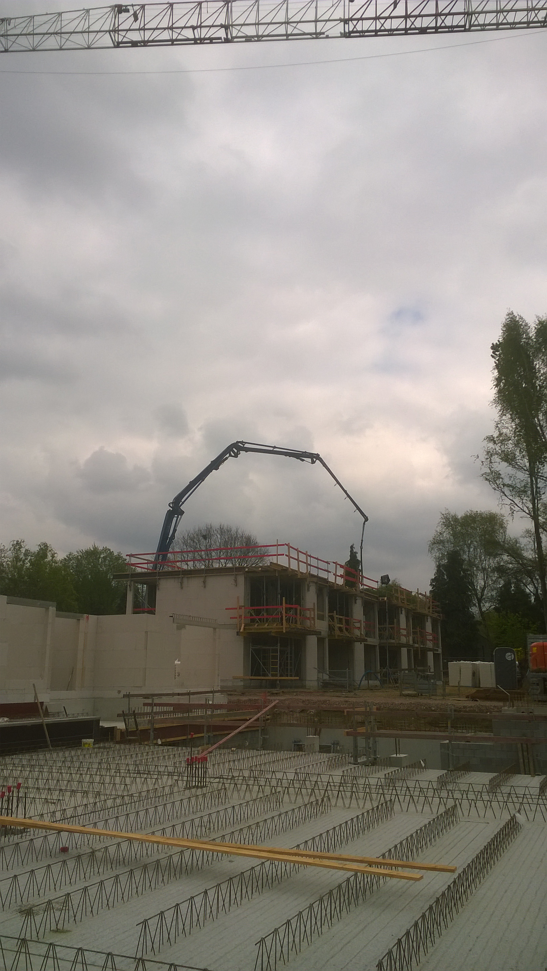 Wylany fundament budynku wielorodzinnego z widocznym zbrojeniem i pompą do betonu na budowie w pochmurny dzień.