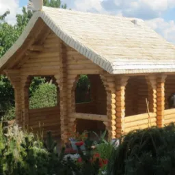 Drewniana altana z dachem krytym gontem bitumicznym, otoczona zielenią. Widoczny detal w postaci rzeźbionego ptaka na szczycie dachu. Zdjęcie z datą w prawym dolnym rogu.