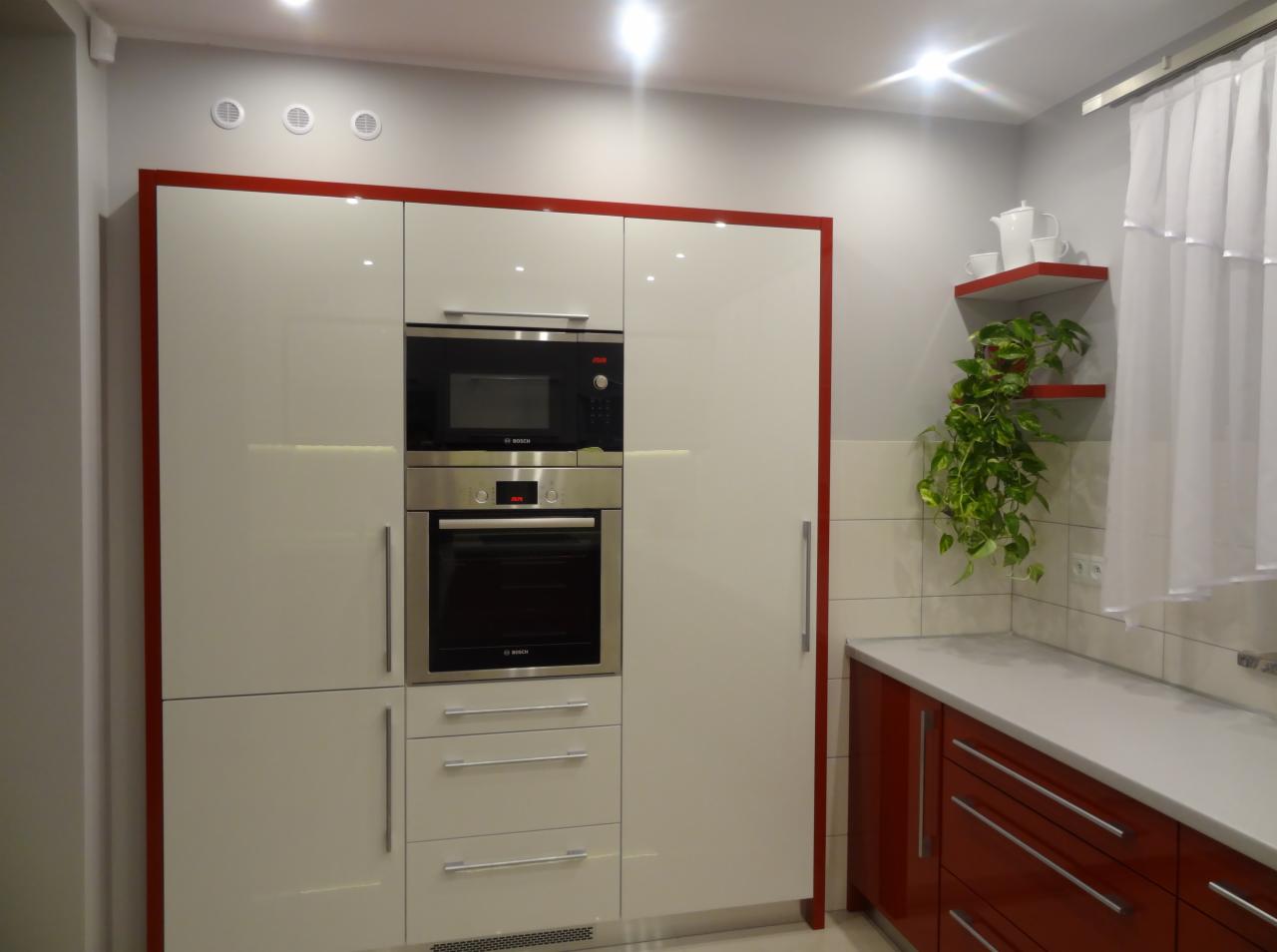 Nowoczesna kuchnia w Świerczowie z białymi szafkami obramowanymi czerwonymi listwami, zabudowanym piekarnikiem i mikrofalówką marki Bosch oraz blatem z rośliną.