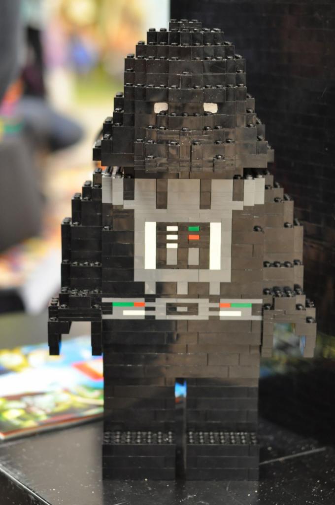 Figurka Dartha Vadera zbudowana z czarnych klocków Lego, z szarymi i białymi elementami na torsie, ustawiona na czarnym blacie.