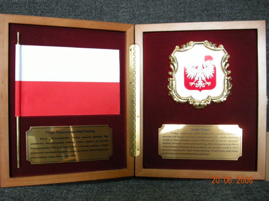 Oprawiona w drewnianą ramkę flaga Polski z tabliczką opisową oraz godło Polski w ozdobnej złotej ramce na czerwonym tle, pamiątka z datą 20.06.2008.