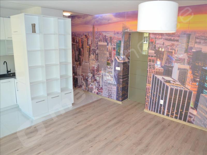 Jasne wnętrze pokoju z panelami podłogowymi, białą zabudową meblową z półkami i szafkami oraz fototapetą z panoramą miasta.