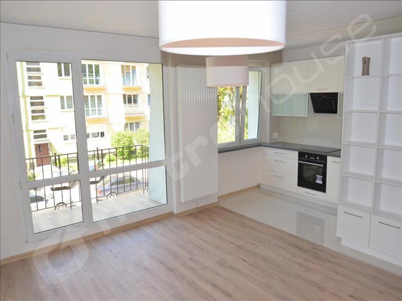 Jasne, przestronne wnętrze nowo wykończonego mieszkania z widokiem na balkon i budynek mieszkalny; widoczna kuchnia w zabudowie z białymi szafkami i sprzętem AGD, panele podłogowe w odcieniach...